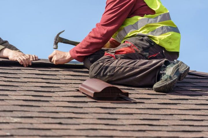 Two skilled roofers in the process of roof installation using a hammer and a nail