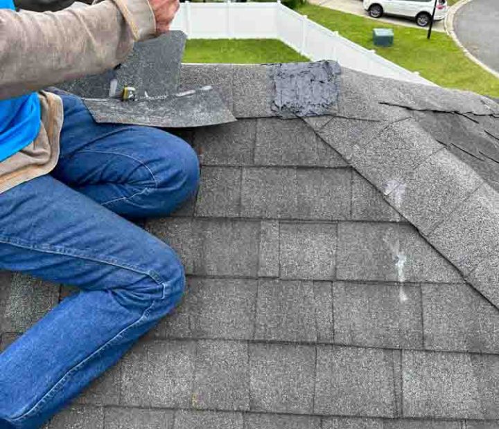 Worker installing asphalt shingle on a roof ridge of a house