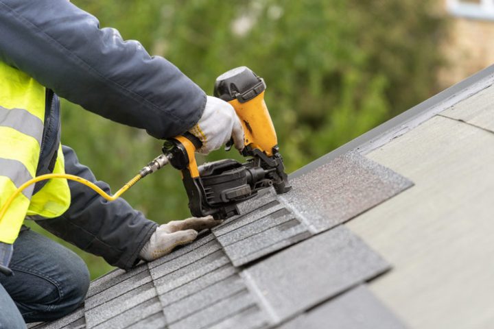 A professional roofer using pneumatic nail gun to install tile on the roof of a house